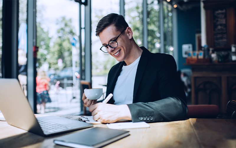 man taking notes while drinking coffee