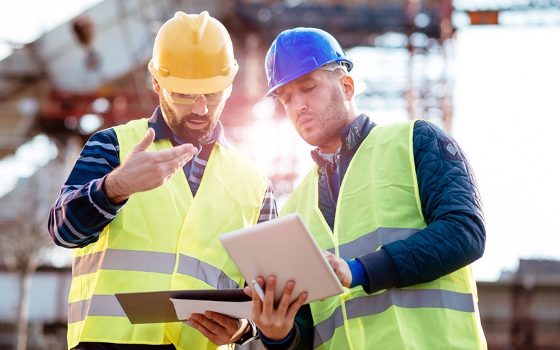 Construction workers in hard hats on site using tablet device